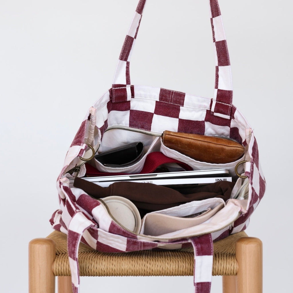 Plaid-patterned bag with sunglasses and a phone inside, held by a hand on a white background.