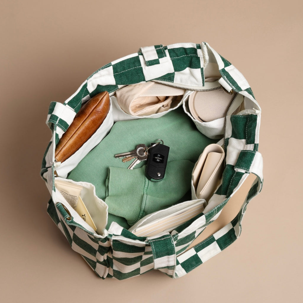 Green and white checkered bag with items like a phone, keys, and a wallet inside on a beige background