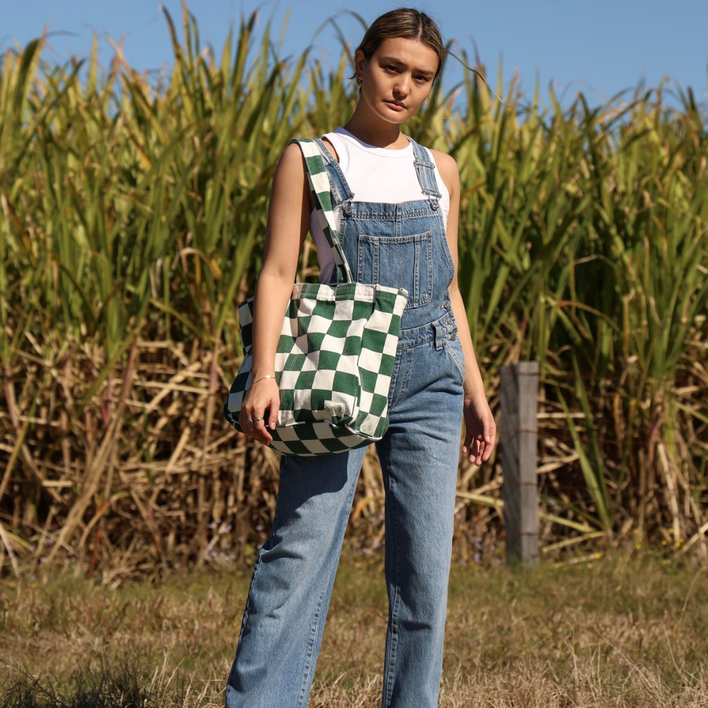 Woman in denim overalls holding a checkered bag in a field