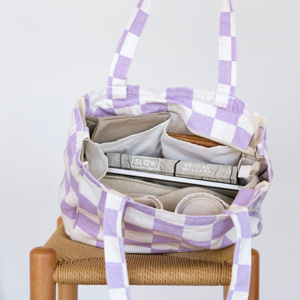 Purple and white checkered bag with items inside, held by a hand on a white background